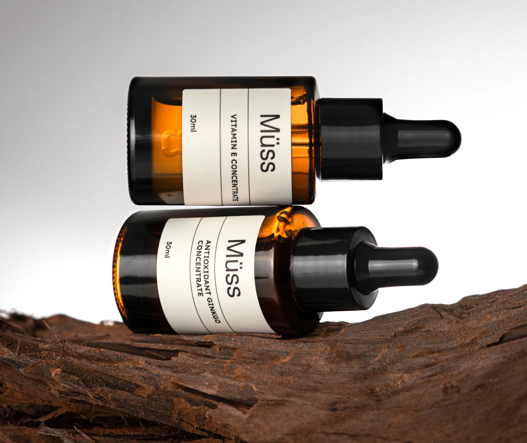 Two amber dropper bottles labeled 'Müss' resting on a piece of dark driftwood