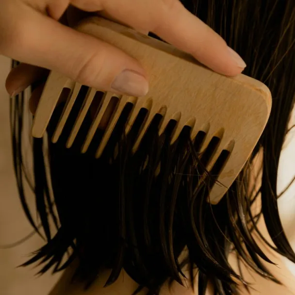 Wooden wide-tooth comb being drawn through hair, representing scalp care