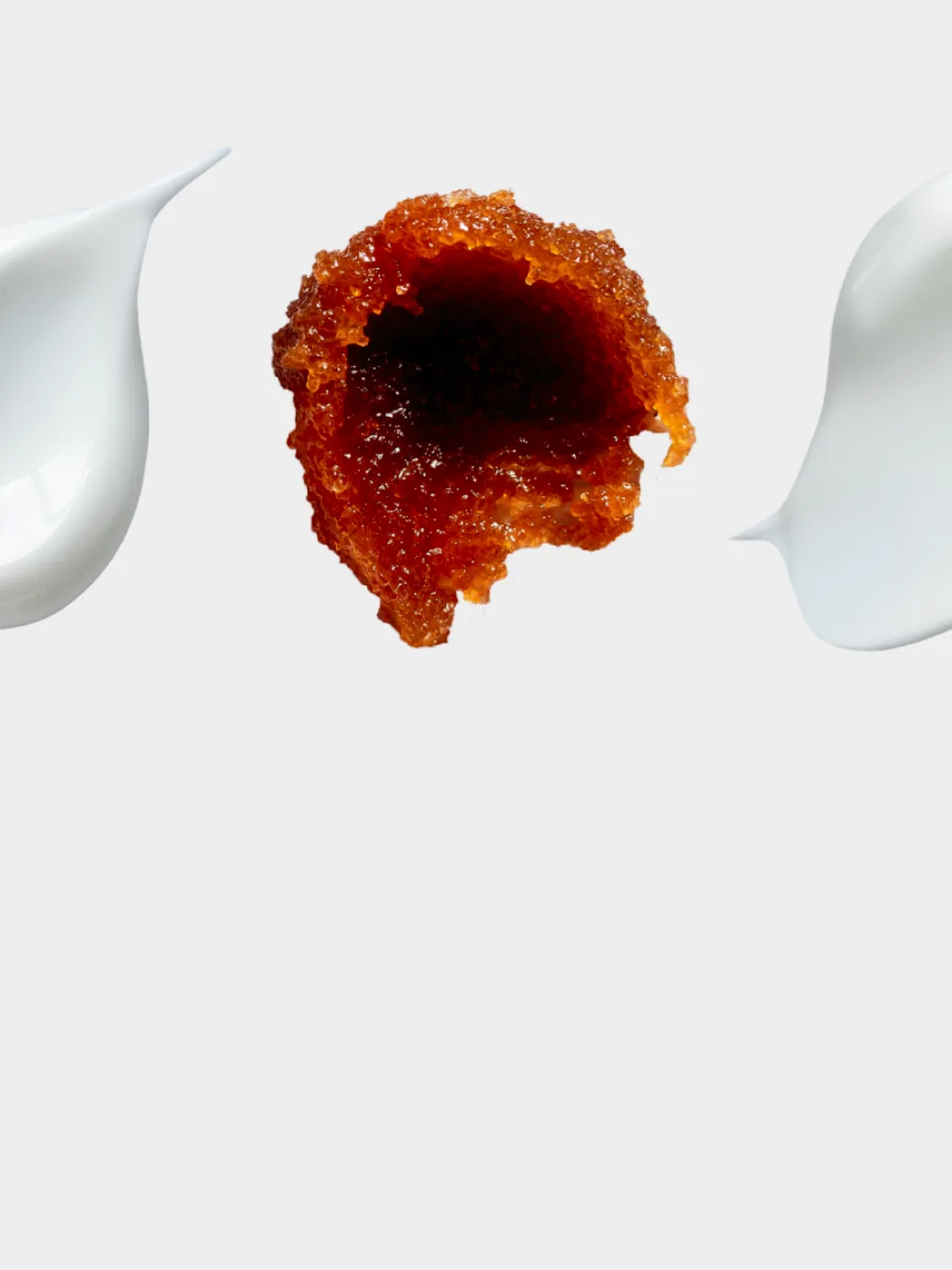 Macro shot of an amber, honeycomb-textured gel with a bite taken out of it, flanked by white cream swooshes