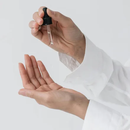 Hands holding an open dropper bottle to test a sample formula
