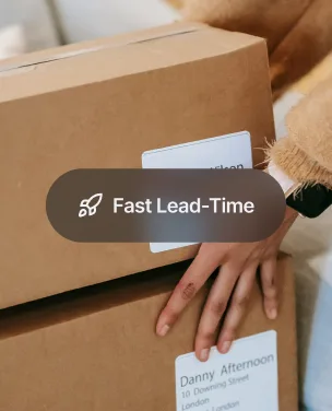 Hand placing a shipping label on a cardboard box marked 'Fast Lead-Time'