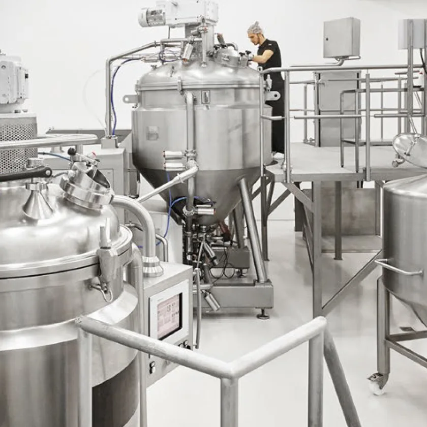 Workers operating stainless steel manufacturing equipment in a cosmetics production facility